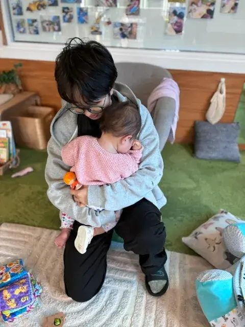 A Growing Minds teacher cuddling a baby in the Fantail Room
