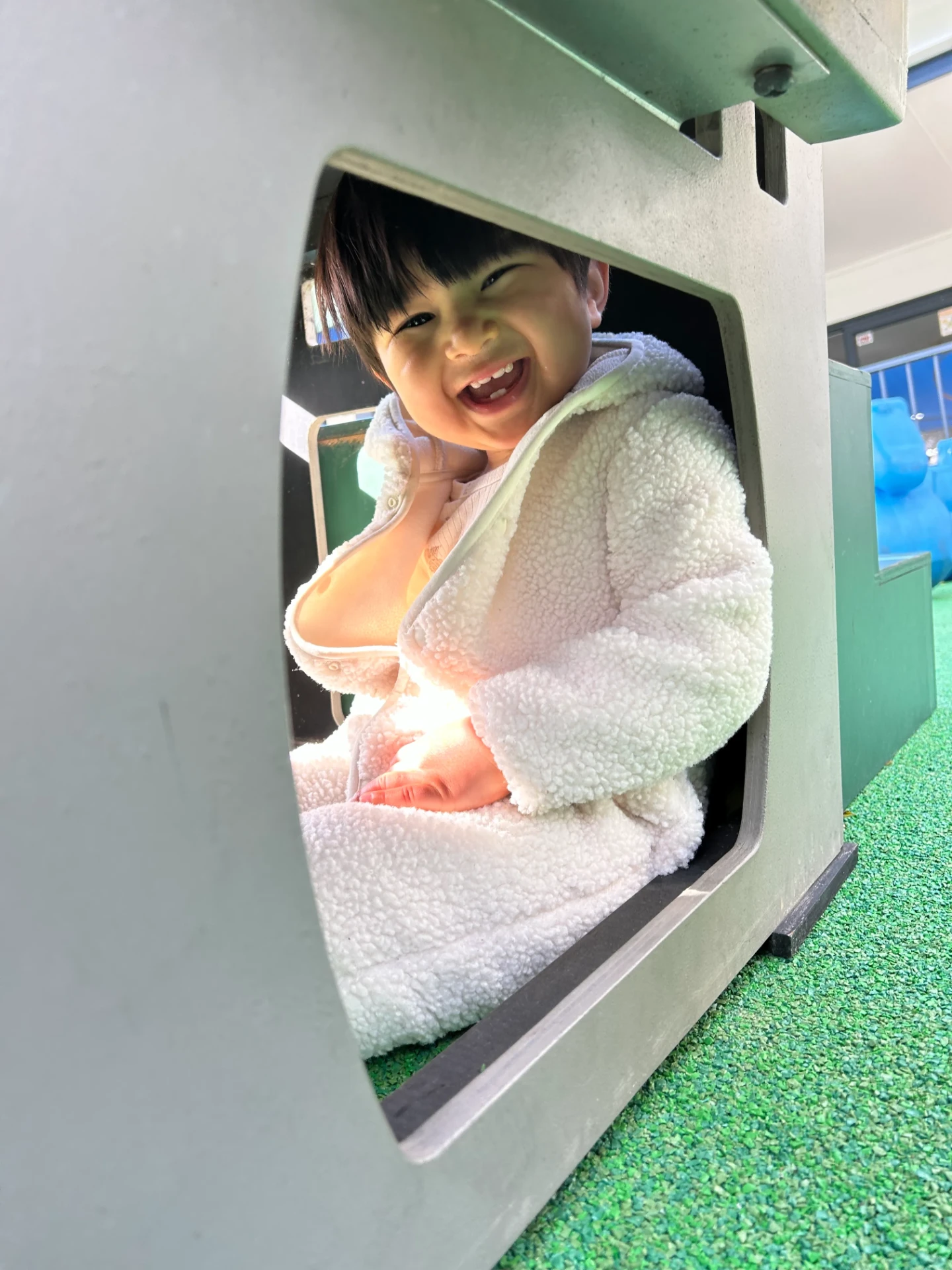 A child laughing while peeking out of the playhouse window at Growing Minds