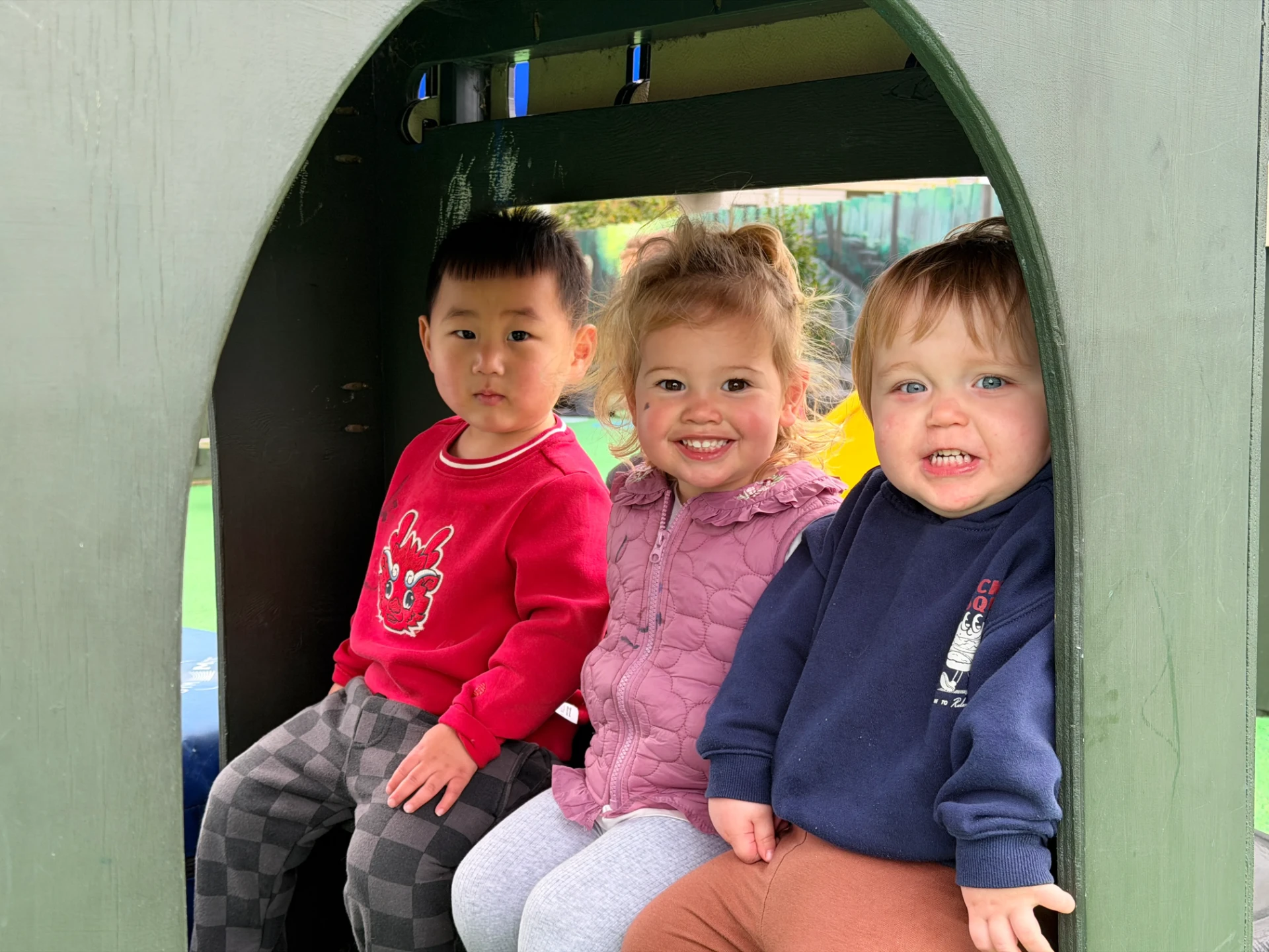 Three toddlers sitting together inside the outdoor playhouse at Growing Minds